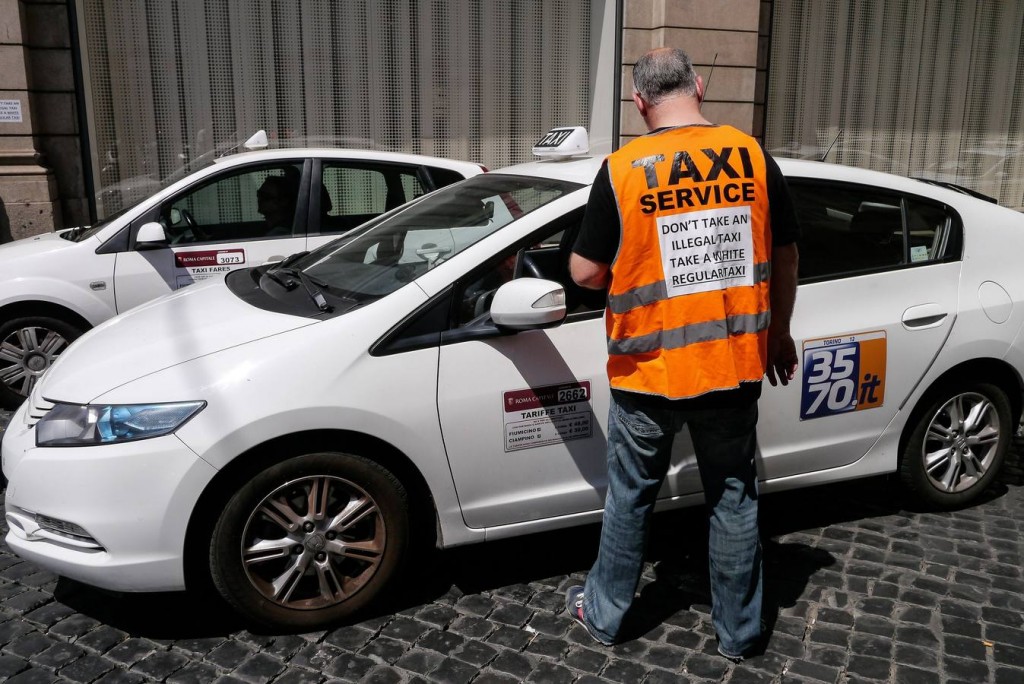 An Italian taxi driver wears a vest reading "Don't take an illegal taxi, take a white regular taxi" during a protest against the growing number of minicabs and cars, known in Italy as Car rental with driver (NCC), on June 11, 2014 in Rome. Taxi drivers in London, Paris and other European capitals plan to bring chaos to the streets today in protest against unlicensed mobile car-hailing services such as Uber which have shaken up the industry.  AFP PHOTO / ANDREAS SOLARO